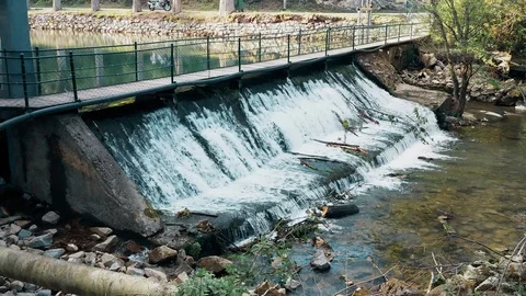 Small artificial waterfall, with a pedestrian bridge 스톡 동영상 107906061