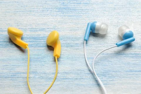 Small assorted multicolored headphones on a light blue wooden background. Stock Photos