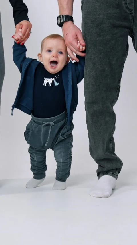 Small baby boy making steps supported by his parents. Family of three wearing Stock Footage 337508160