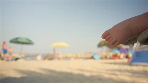 Small baby foot hanging from a stroller, gazing at a blurred sandy beach with 動画素材 343556852