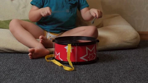 Small baby is playing a drum sitting on the floor alone at home Stock Footage 154101488