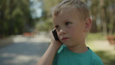Small baby using a small phone in a park. Kid talking on an old telephone Stock-Footage 343208656