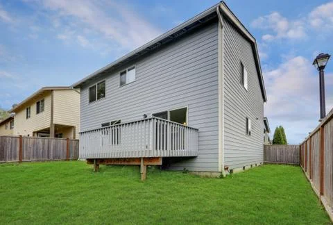 Small back yard with green grass and wooden fence. Gray house exterior.  Nort Stock Photos