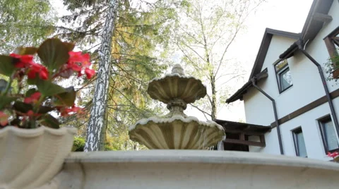 Small backyard fountain decorated with red flowers in a garden near outdoor Stock Footage 63356342