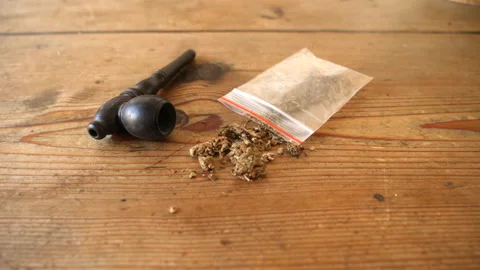 Small bag of marijuana and smoking pipe on table. Dolly reveal shot. Video stock 344742810