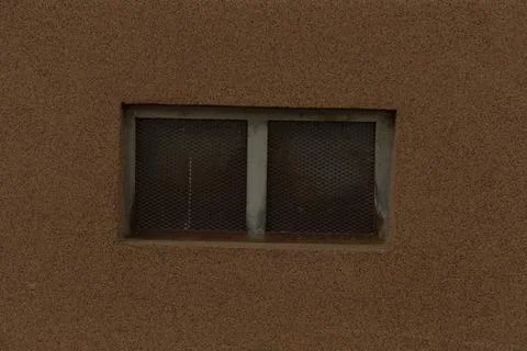 Small barred basement window set in textured brown stucco wall Stock Photos