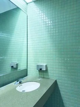 A small bathroom space features green tiled walls and a sink. A mirror reflec 스톡 사진