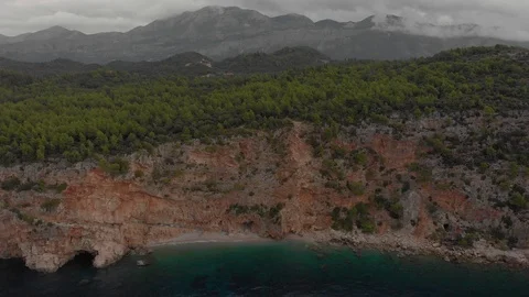 Small beach at the foot of steep cliff. Green forest above sea waters. Cloudy Stock Footage 126242876