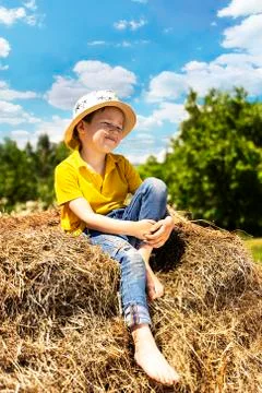 A small beautiful boy is sitting in a hat in the straw Stock Photos
