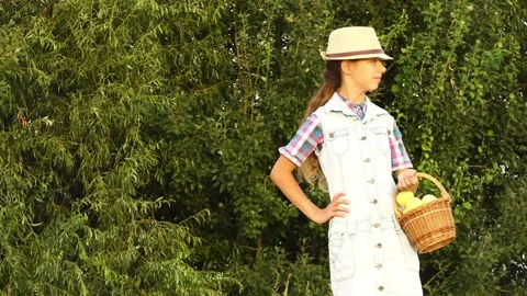 Small beautiful girl in hat holds in her hands wicker basket with apples agai Stock Footage 214992953