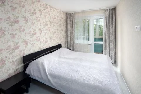 Small bedroom with simple bed with bedspread and flowered walls and curtains Stock Photos