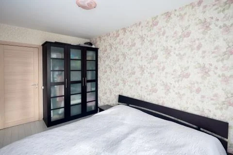 Small bedroom with simple bed with bedspread and flowered walls and curtains Foto stock