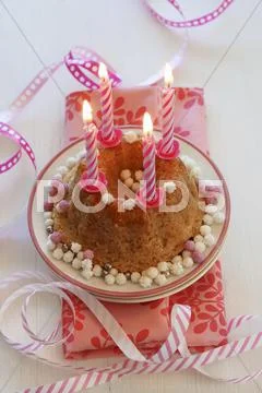 A Small Birthday Cake With Lit Candles And Streamers