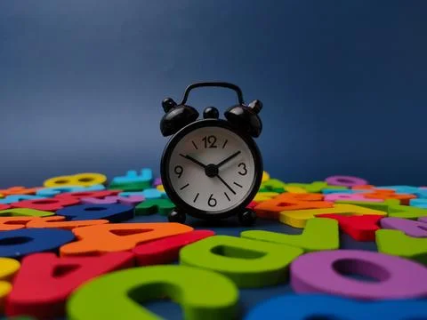 Small black alarm clock standing upright on a bed of colorful wooden letter.. Stock Photos