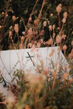 Small black cross on a flat white gravestone. Orange mood overgrown with dry  Stock Photos