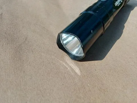 Small black flashlight, on a brown background. Stockfoto's