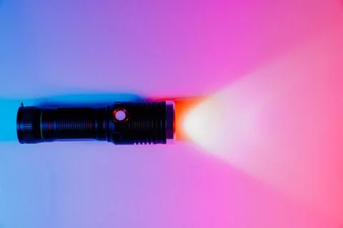 A small black flashlight in colored lighting. Stock Photos