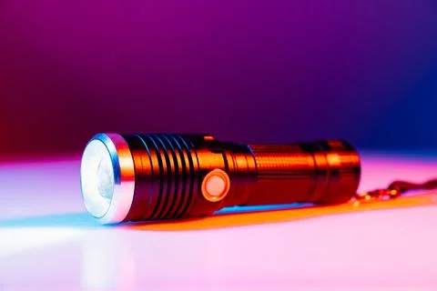 A small black flashlight in colored lighting. Stock Photos