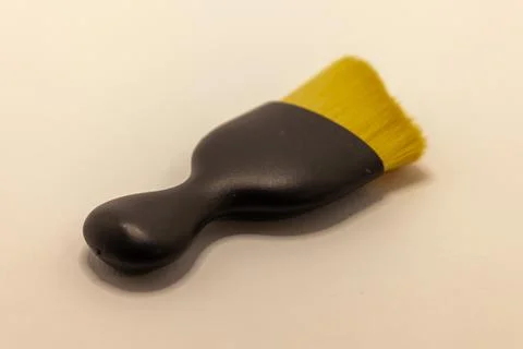 A small, black-handled brush with bright yellow bristles rests on a light, ne Stock Photos