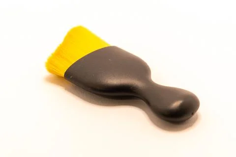 A small, black-handled brush with bright yellow bristles rests on a clean whi Stock Photos