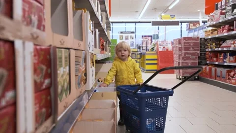 A small blond child himself carries a plastic basket in a supermarket, chooses a Stock Footage 231144390