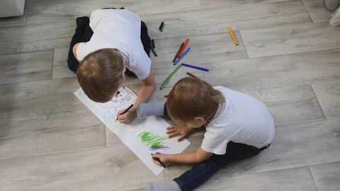 Small blond children sit on the floor and draw on white paper, color with Stock Footage 124846595
