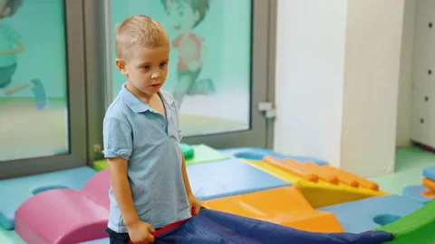 Small blond white boy in nursery holding rainbow play parachute during playtime Stock Footage 219513975