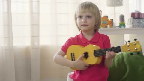 Small blonde kid boy imitate artist playing toy guitar dreaming to become Video stock 78296328
