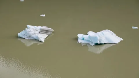 Small blue icebergs floating and drifting slowly in murky glacial water Видео 335299349