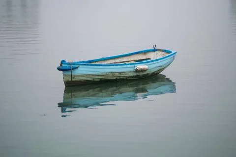 Small blue rowing boat floating on water in the mist and fog Foto stock