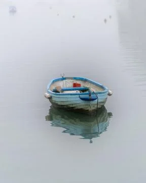 Small blue rowing boat floating on water in the mist and fog Foto stock