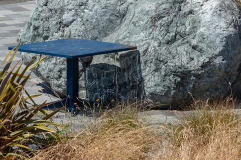 Small blue rusty table sitting near large boulder and grassy weeds Stock Photos