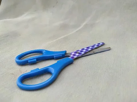 Small blue scissors with purple handle on light fabric Photos