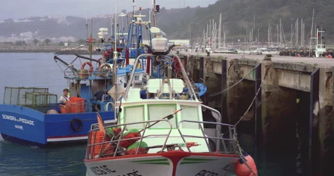 Small blue ship docking in harbour near other boats during cloudy day Stock Footage 158645018