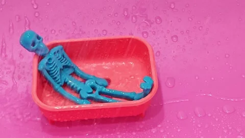 Small blue skeleton relaxes in a red tray while water splashes around Stock Footage 338120733