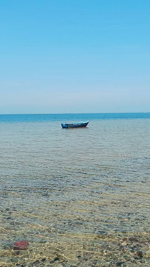 Small blue wooden boat floating on calm shallow sea water under clear blue sky. Stock Footage 310745895