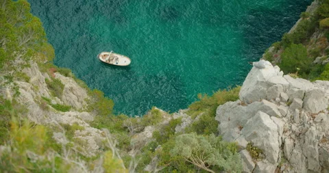 Small boat and seagull beneath steep rocky cliff above calm turquoise sea in Stock Footage 344753344