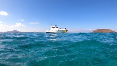 Small boat floating on ocean with blue sky and mountains in background Vídeo Stock 206333969