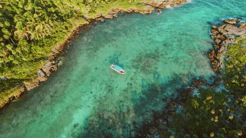 Small boat floating in turquoise bay by tropical palm forest and rocky coast Video stock 326033730