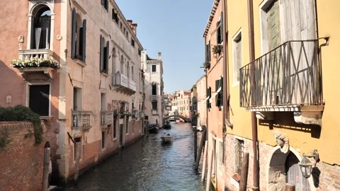 A small boat glides through a sunlit Venetian canal flanked by pastel buildings. Vidéo 314667619