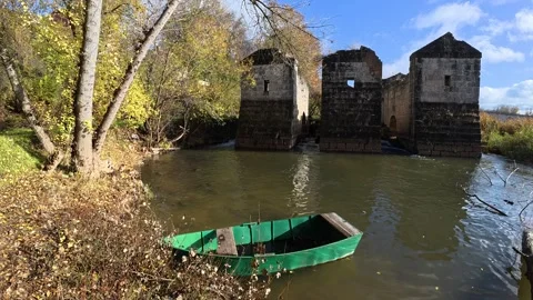 A small boat moored on the river next to the ruins of an old stone mill Stock Footage 322183035