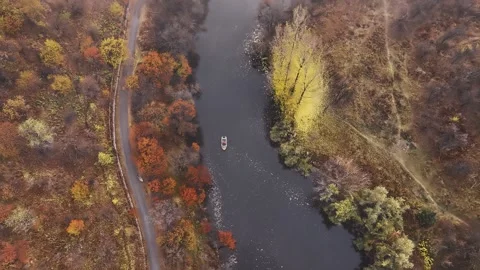 Small boat navigating a calm river amidst autumn foliage Stock Footage 315556519