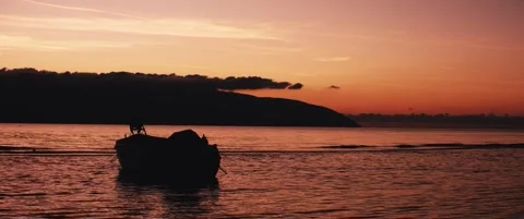 A small boat resting on calm waves at sunset Stock Footage 324460442