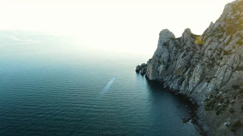 A small boat sails along the rocks at sunset Vídeo Stock 167133638