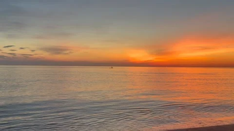 Small boat sails toward glowing sunrise across calm sea. Golden morning light Видео 337777108
