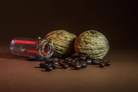 A small bottle with coffee beans and walnuts on a brown background Stock Photos