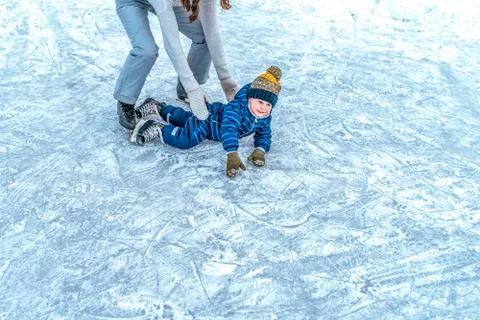 A small boy 2-5 years old, fell on the ice in the winter ice skating. Mom raises Stock Photos