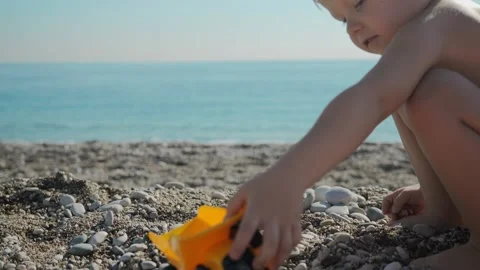A small boy of 5 years old is playing on the beach near the sea with a toy truck Stock Footage 229276133
