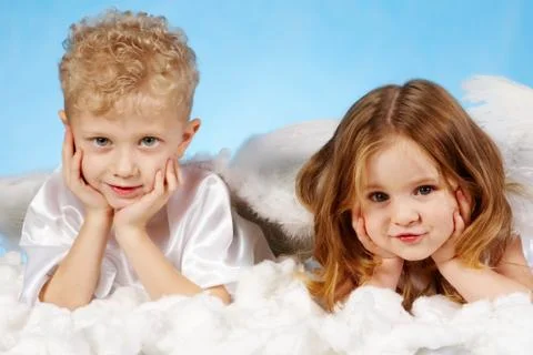 Small boy and girl in angelic costume lying on white cloud Stock Photos