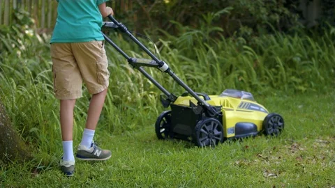 Small boy cuts grass with a green electric lawn mower Stockbeeldmateriaal 109553382